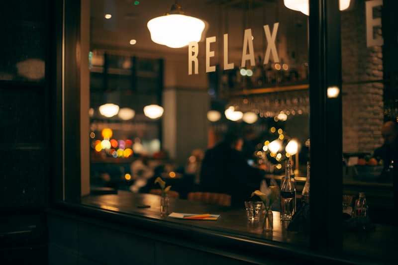 The café seen from the street after dark, warm lamplight behind glass lettering reading RELAX.