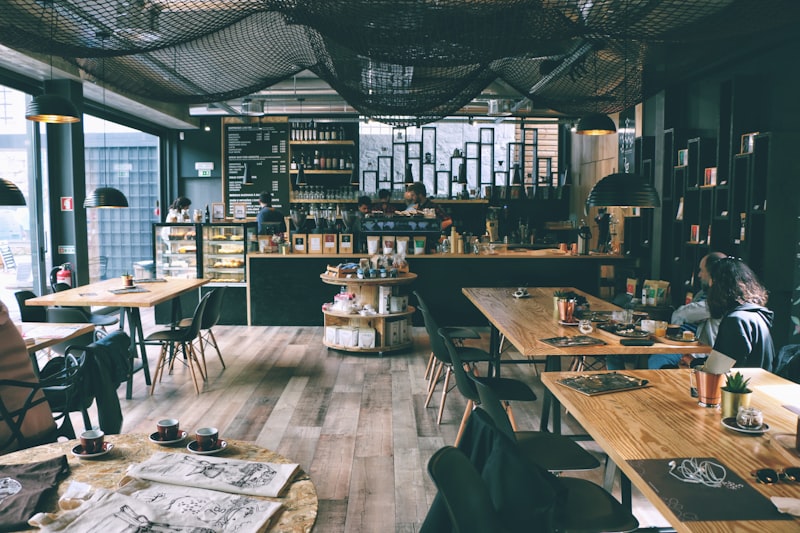 The café floor at dusk: long wooden tables, black chairs and low pendant lamps over the espresso counter.