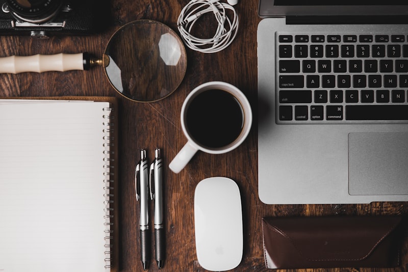 A laptop, notebook, and coffee cup laid out on a wooden desk, overhead view
