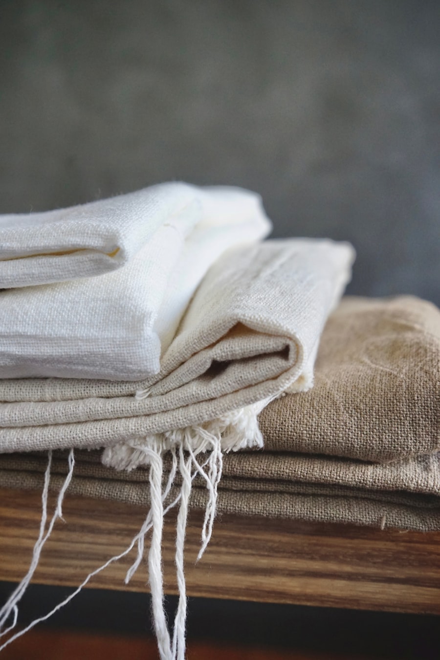 Folded linen throws in cream and stone, stacked on a bench