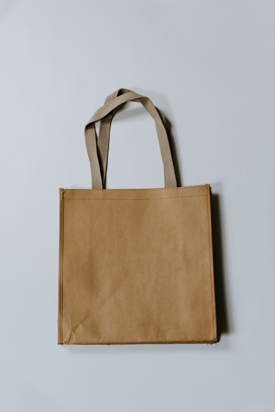 A plain canvas tote bag with fabric handles, hanging against a light wall