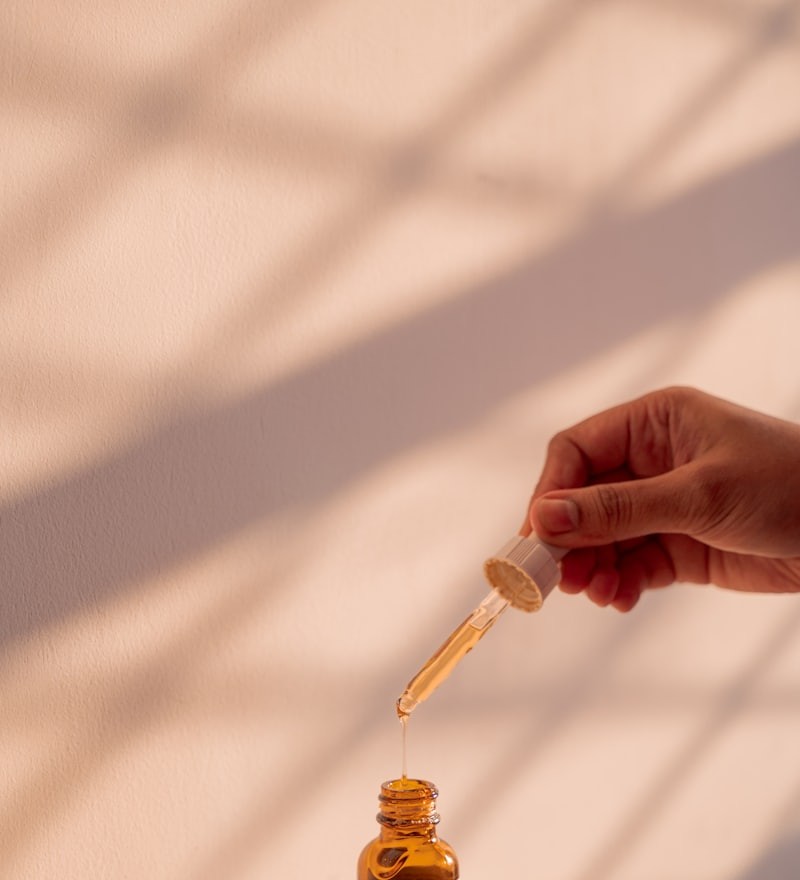 A dropper of skincare serum held above an amber bottle, wide framing with warm afternoon light