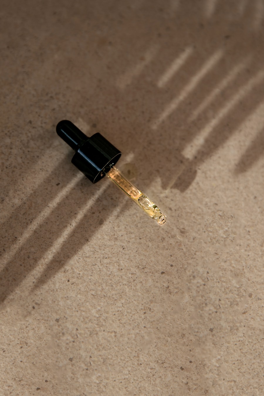 A glass pipette of serum lying on pale stone, crossed by hard shadows from a window blind