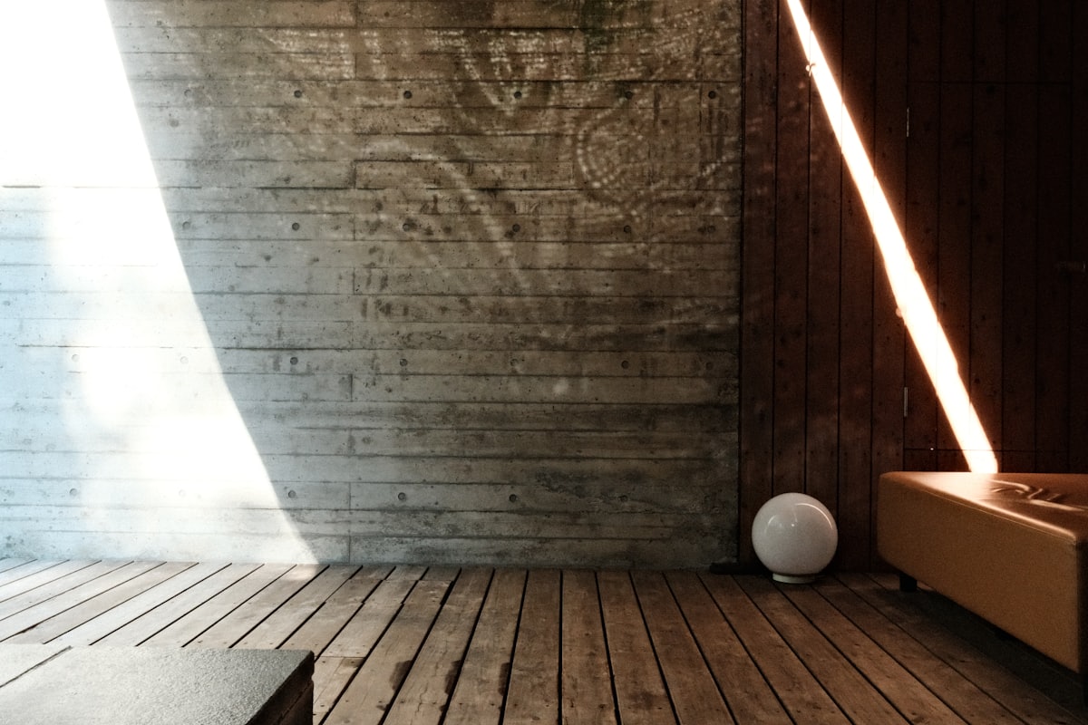 Late afternoon light falling across a bare concrete wall and a wooden floor