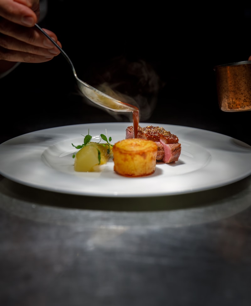 A chef's hands finishing a plated dish tableside under low kitchen light