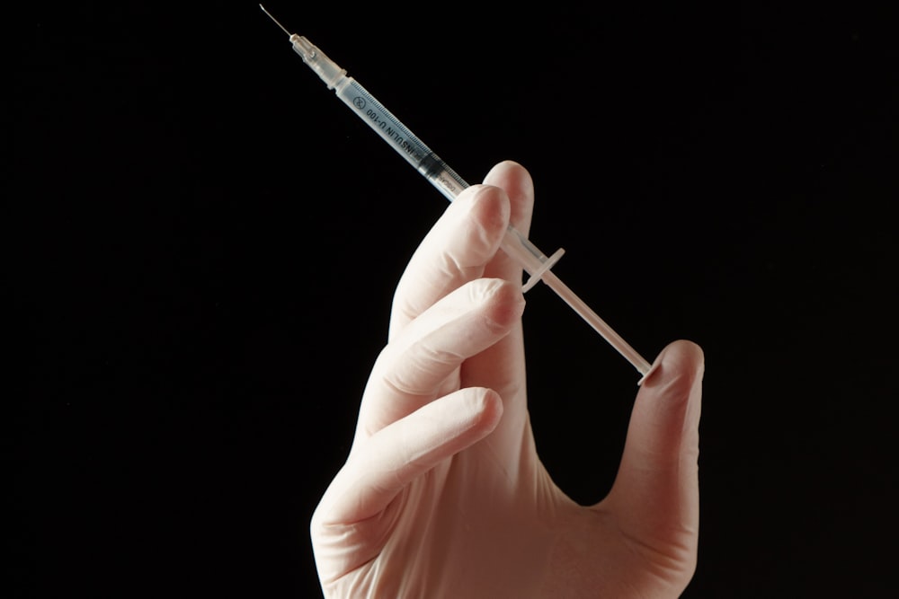 A gloved hand holding a syringe against a dark background